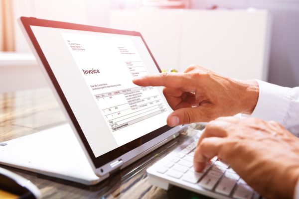 Close-up Of A Businessperson's Hand Analyzing Invoice On Laptop